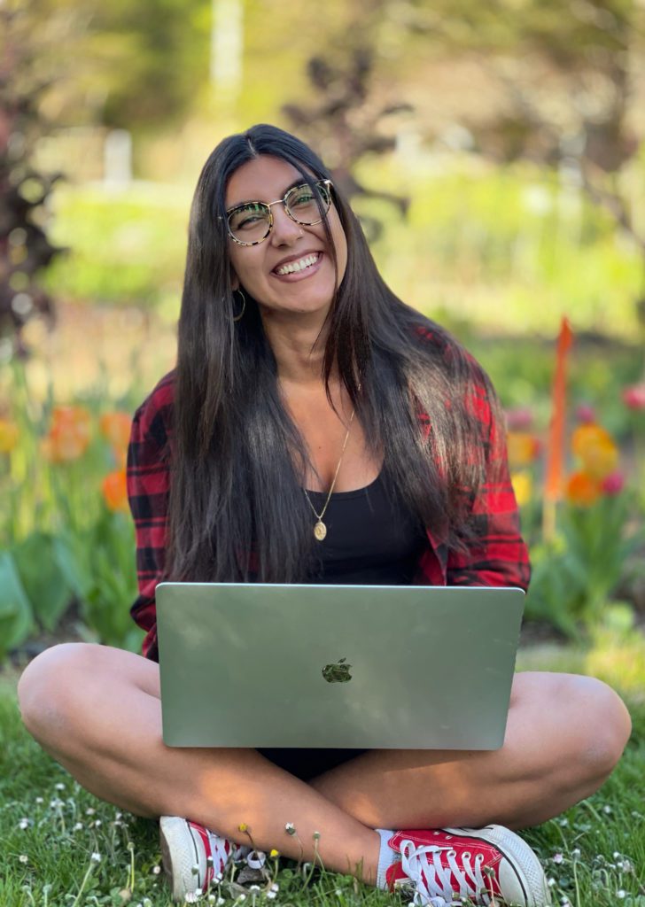 A happy student from the SVIW Virtual Hollyhock program sitting on the garden floor